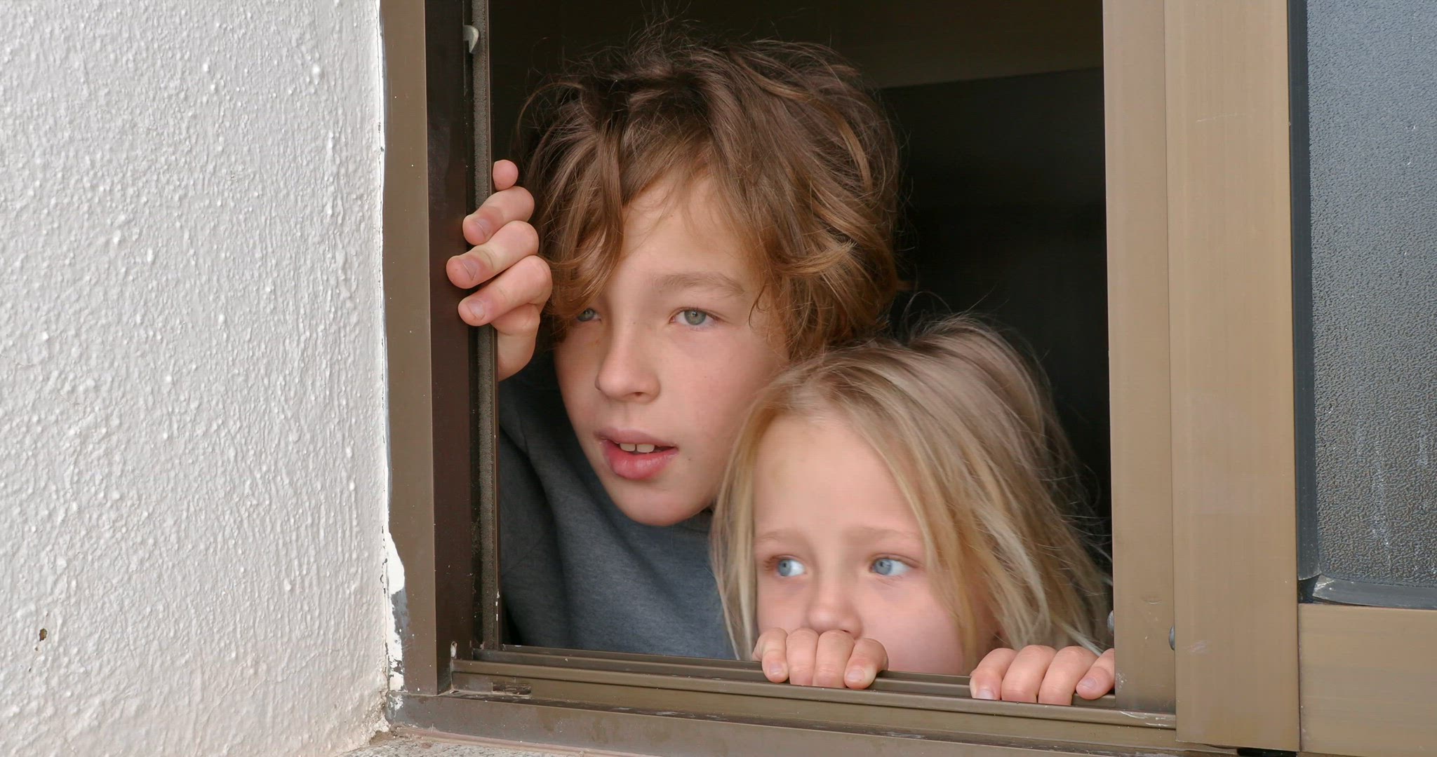 Sister and brother looking outside through the open house window
