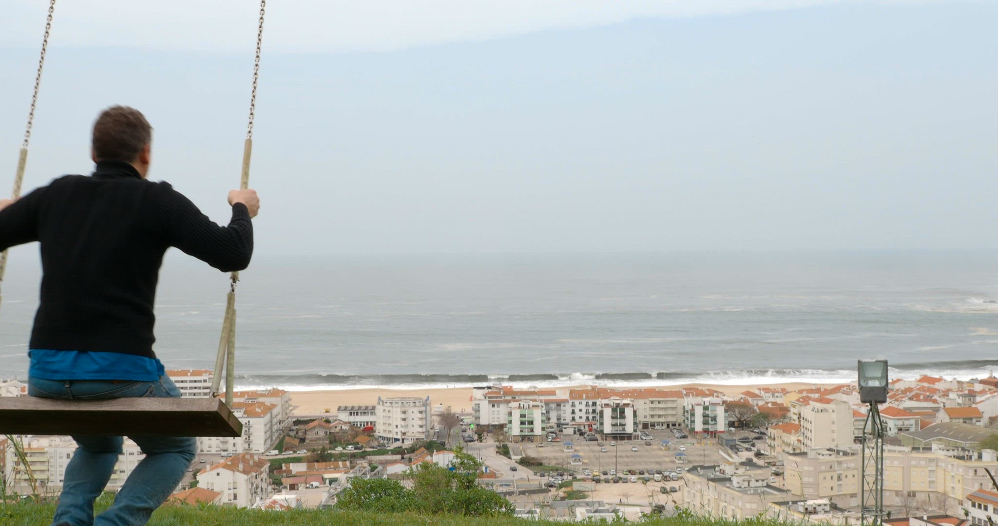 Man swinging on the hill overlooking resort town and ocean. Nazare in Portugal