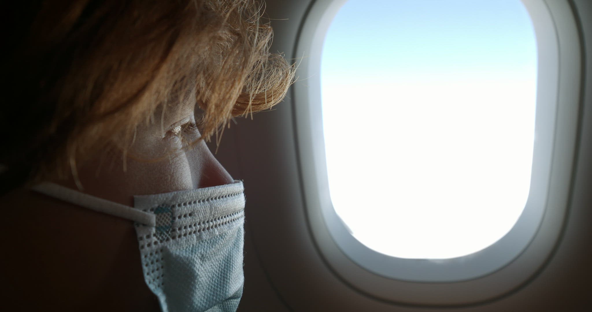 Boy in mask looking through the plane window