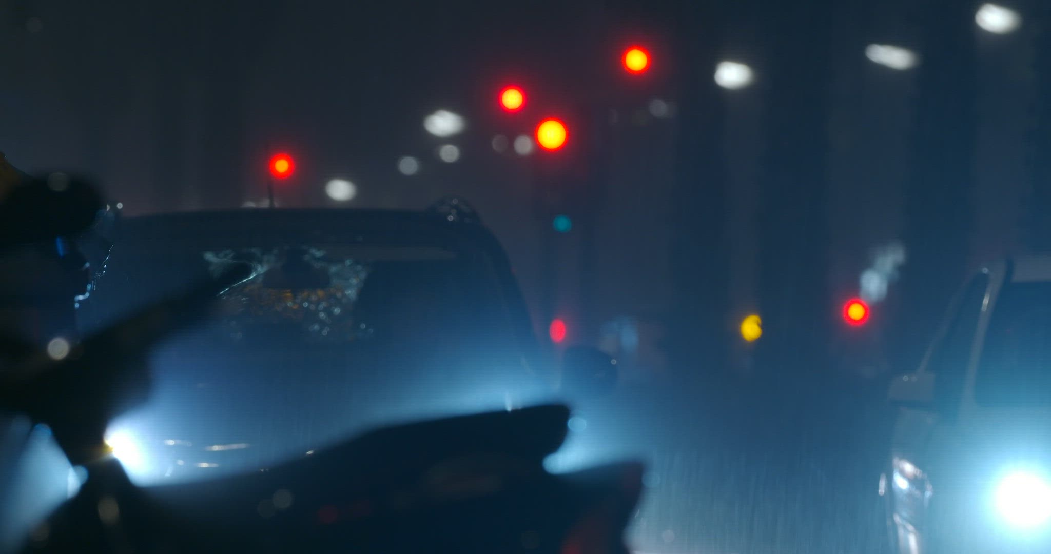 Car with dazzle lights moving slowly in night city under the rain