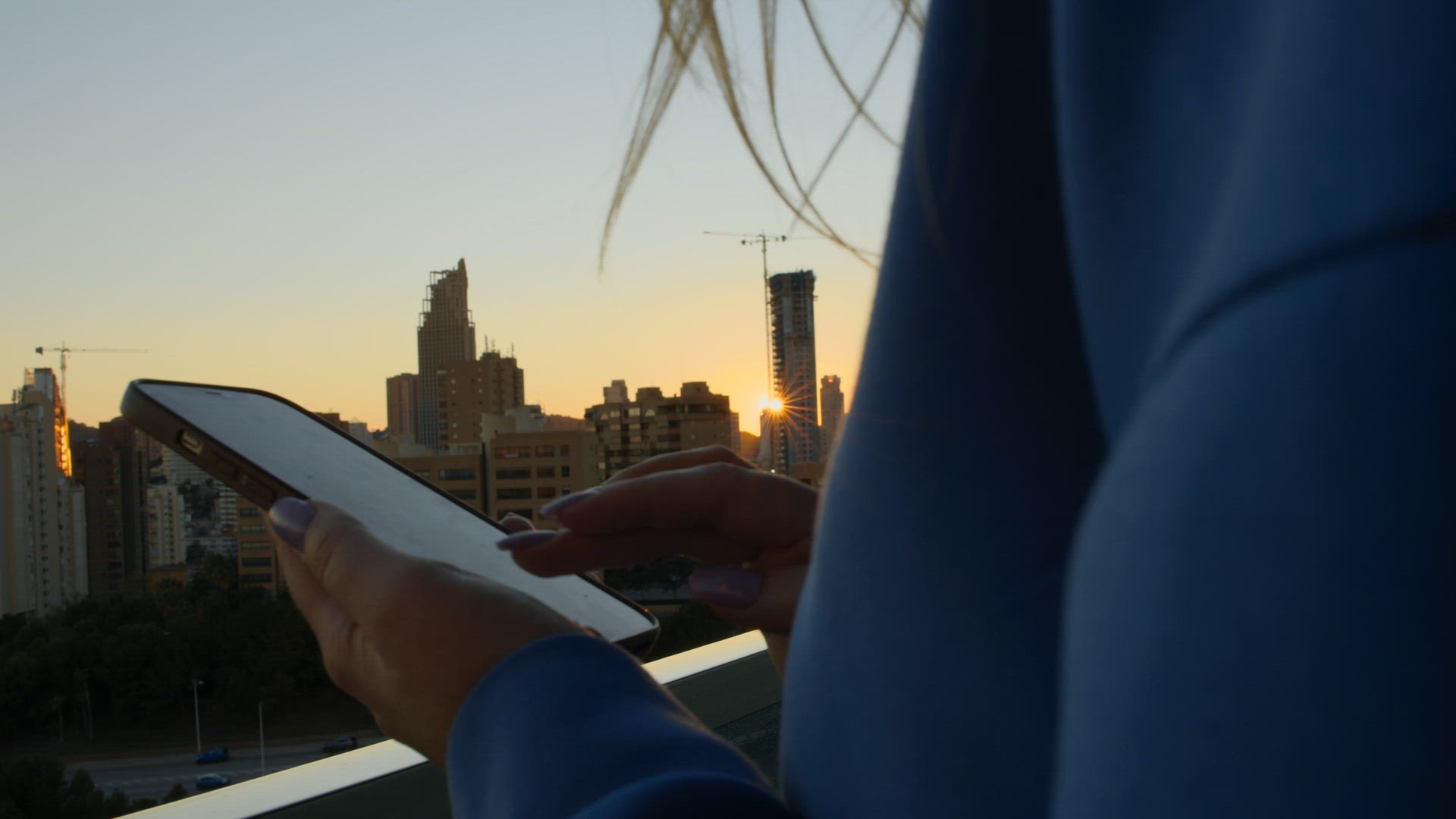 Woman texting on mobile against morning cityscape with rising sun