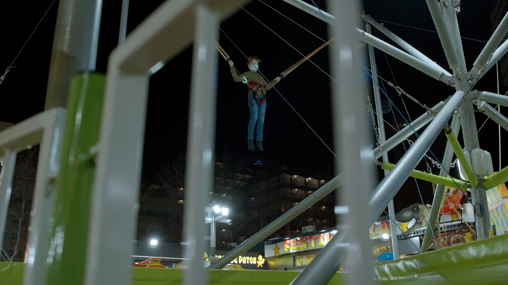 Boy jumping on bungee trampoline in funfair at night