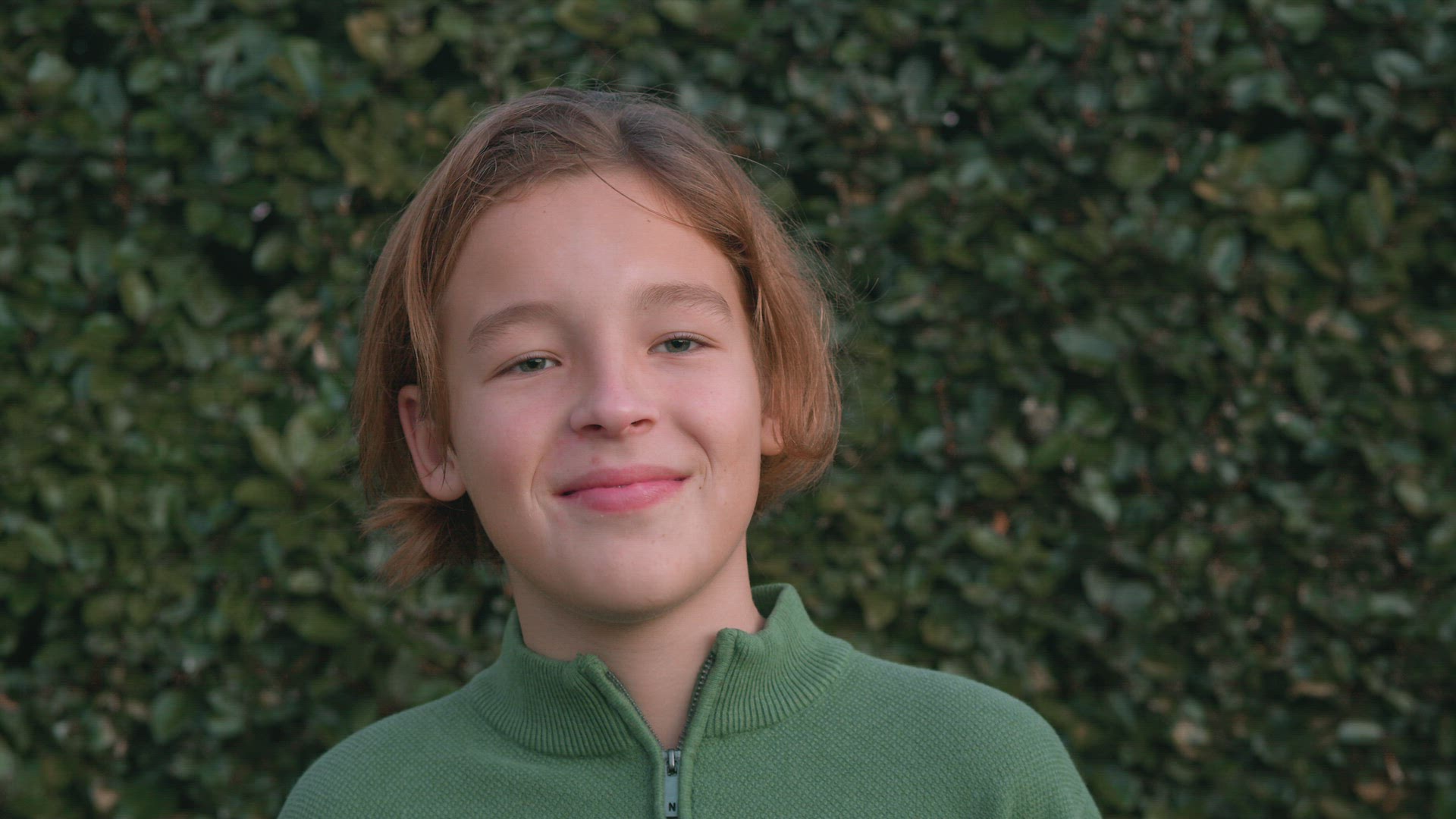 Boy Laughing by a Leafy Fence