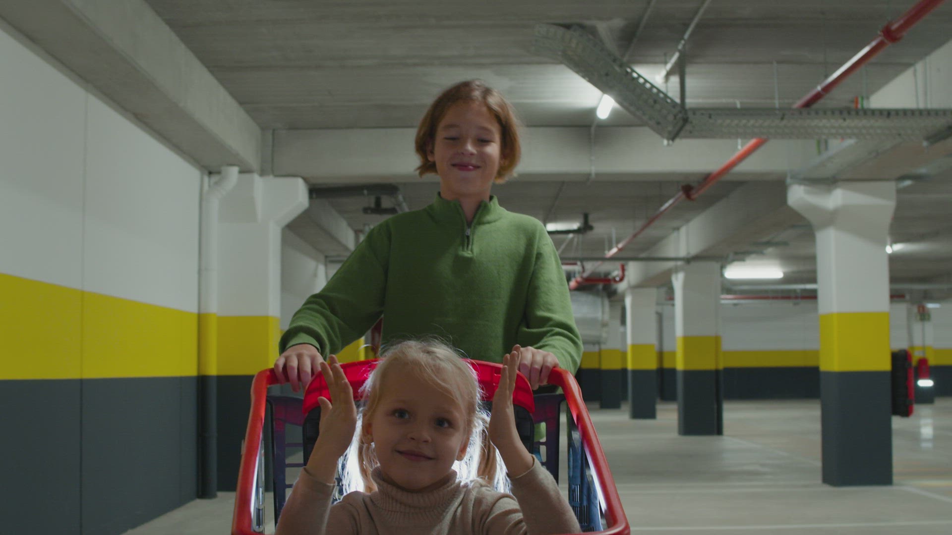Siblings having fun: brother pushing sister in shopping cart on supermarket parking lot