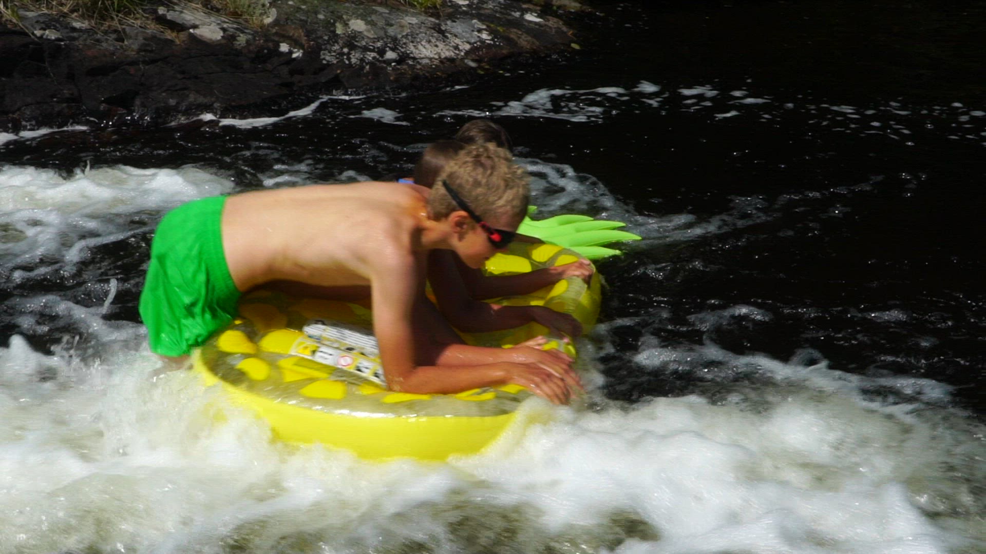 Three children playing on air mattress in river