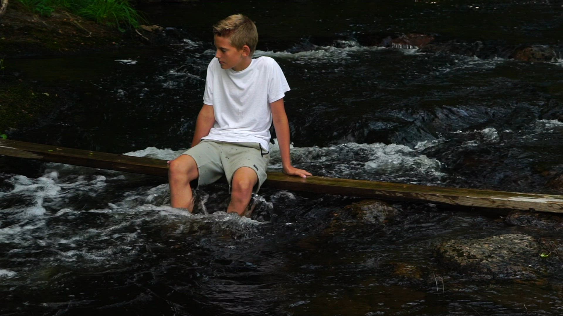 boy in white t-shirt sitting on plank i river - slow motion shot