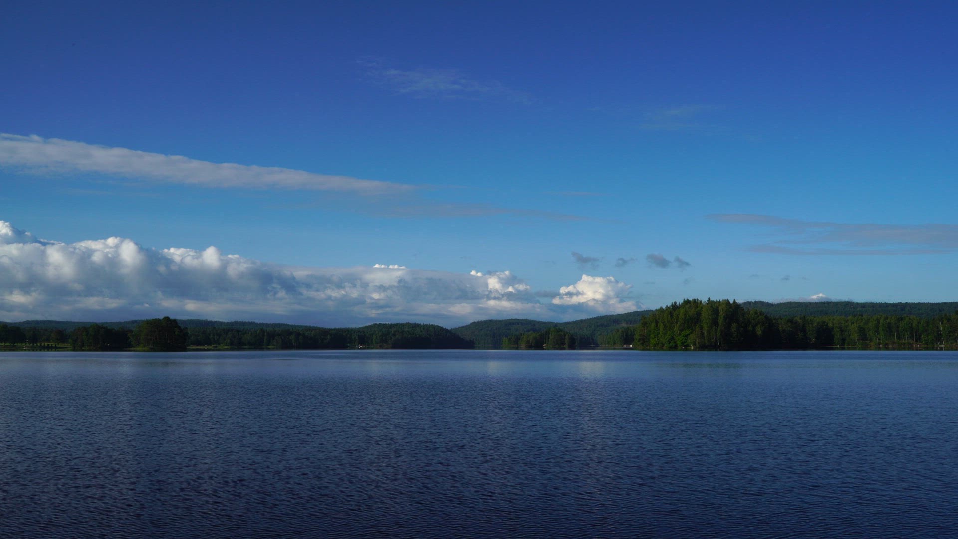 view over lake in värmland - forests in background - blue sky - ripples in lakes water