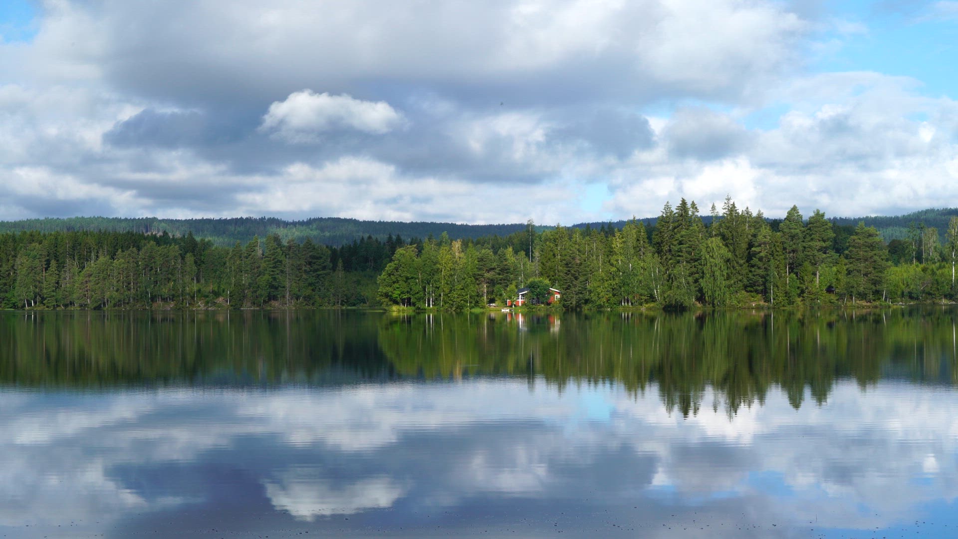 red summer cottage in forest close to lake - ripples in lake water - reflections in water