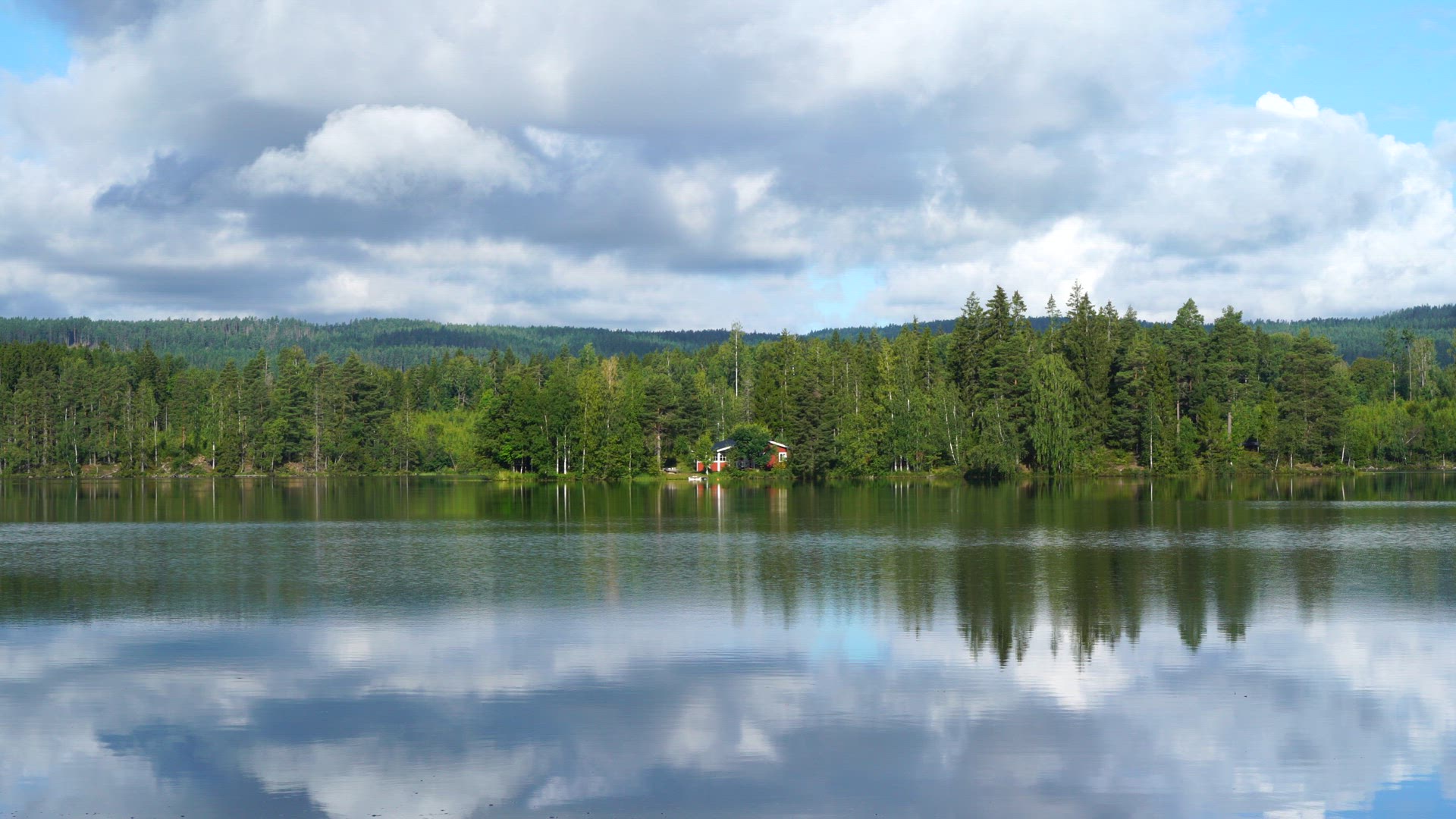 red summer cottage in forest close to lake - ripples in lake water - reflections in water