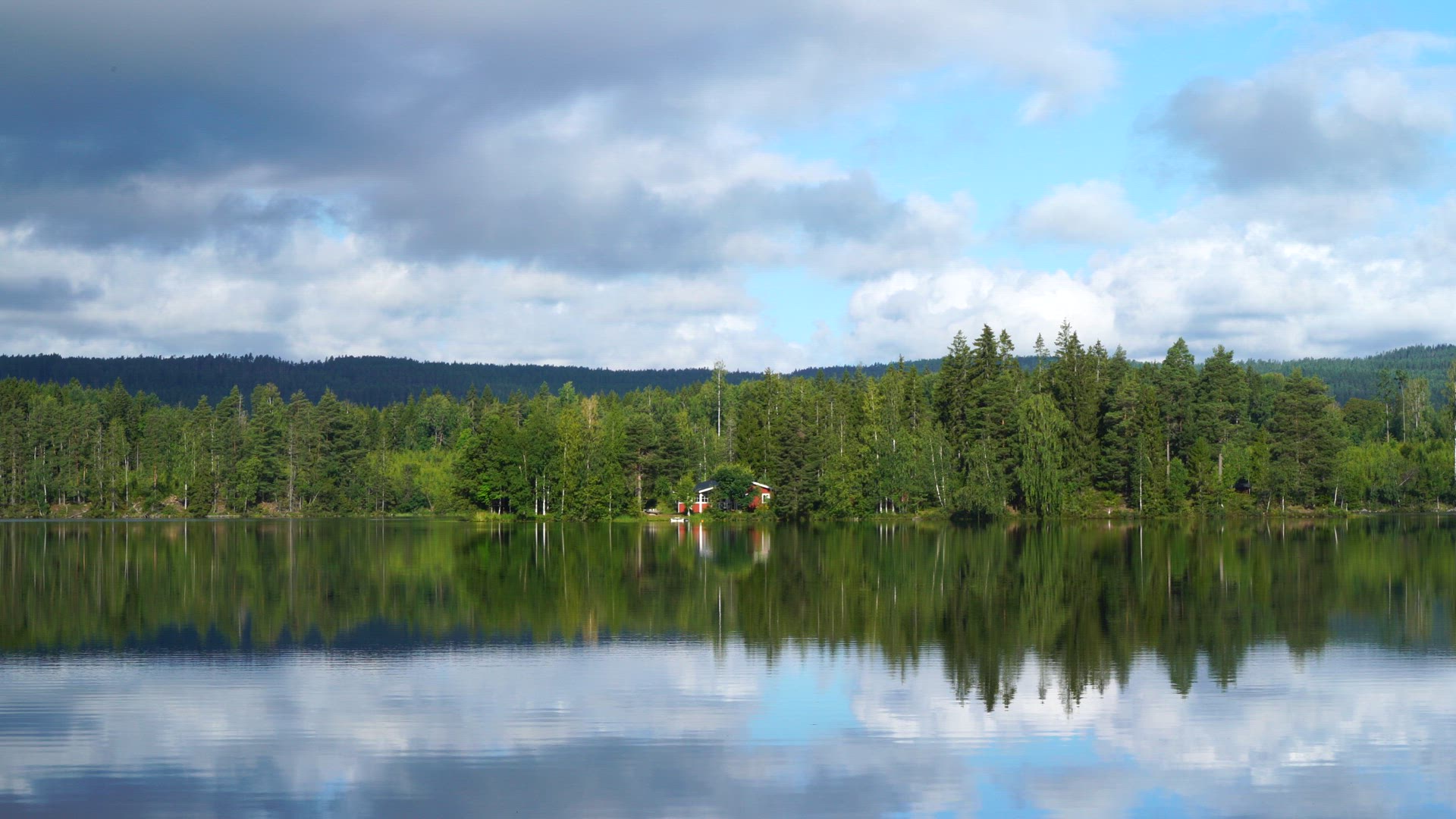 red summer cottage in forest close to lake - ripples in lake water - reflections in water