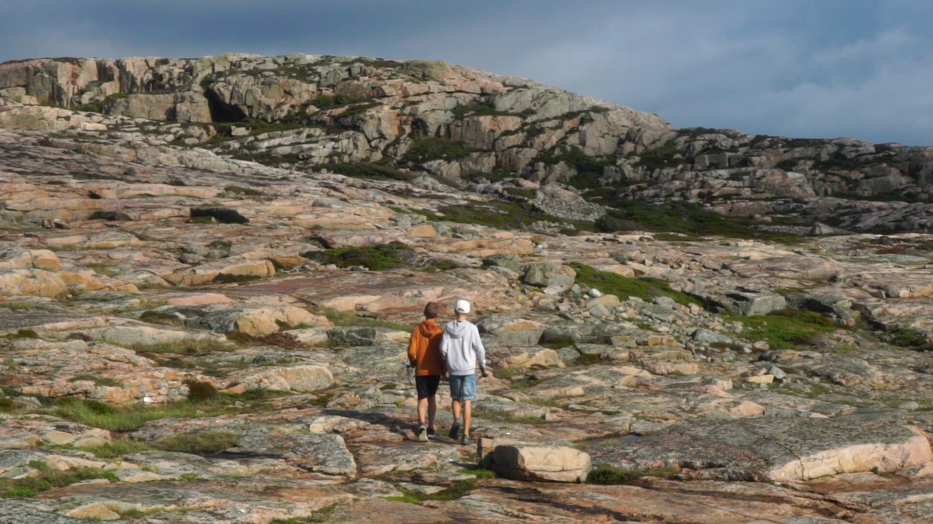 two boys walking on cliffs in Bohuslän - carrying one fish and one fishing rod
