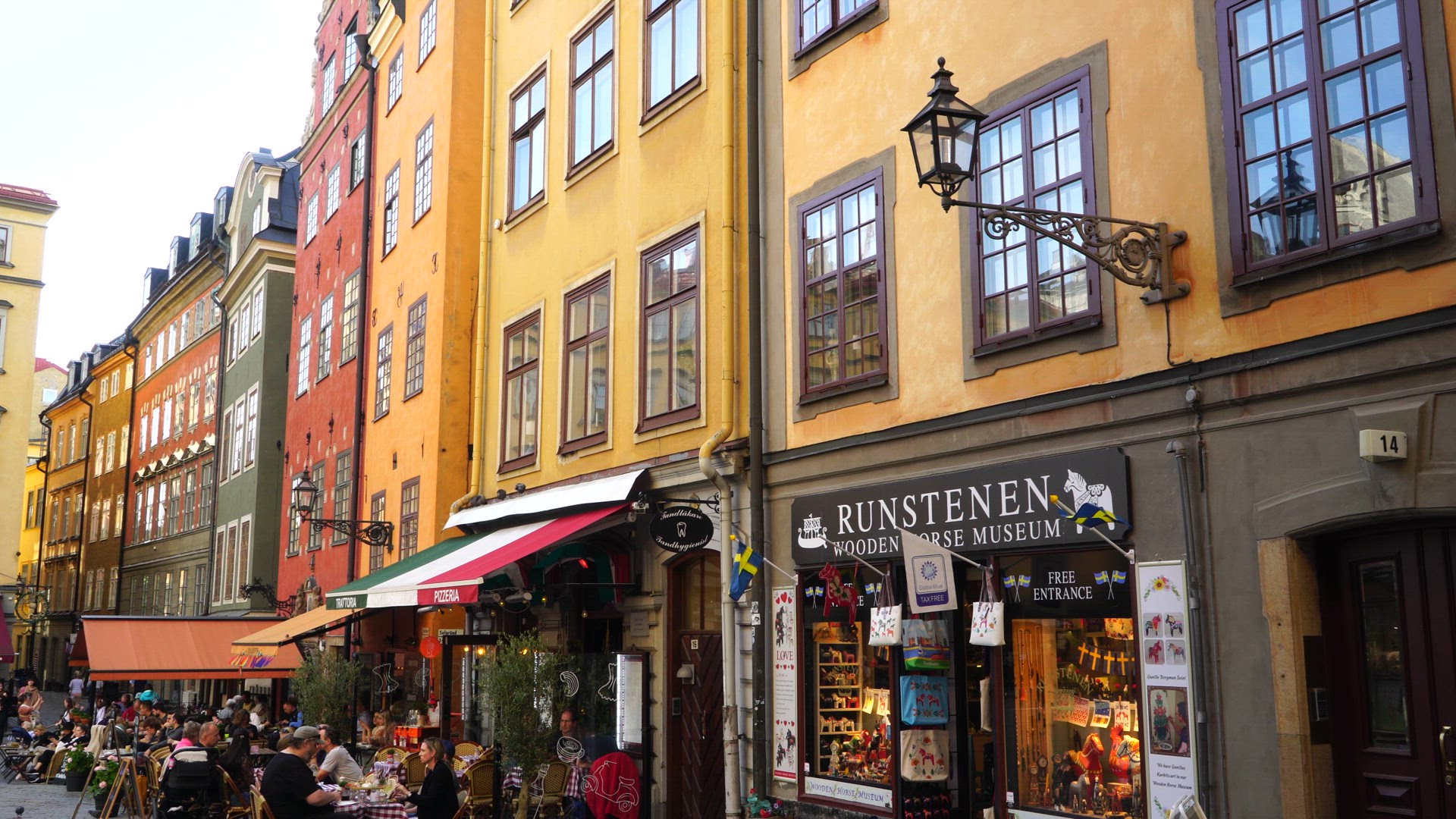 facades of buildings in old town in stockholm - restaurants with people - cyclists passing