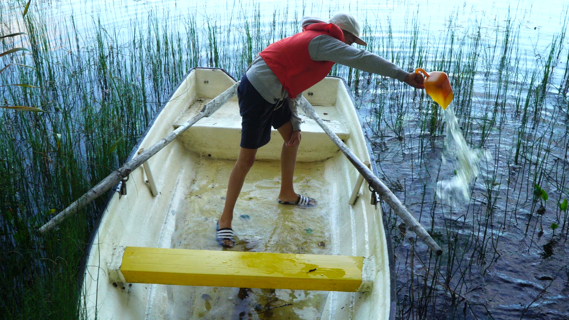 boy scooping water out of small boat - row boat