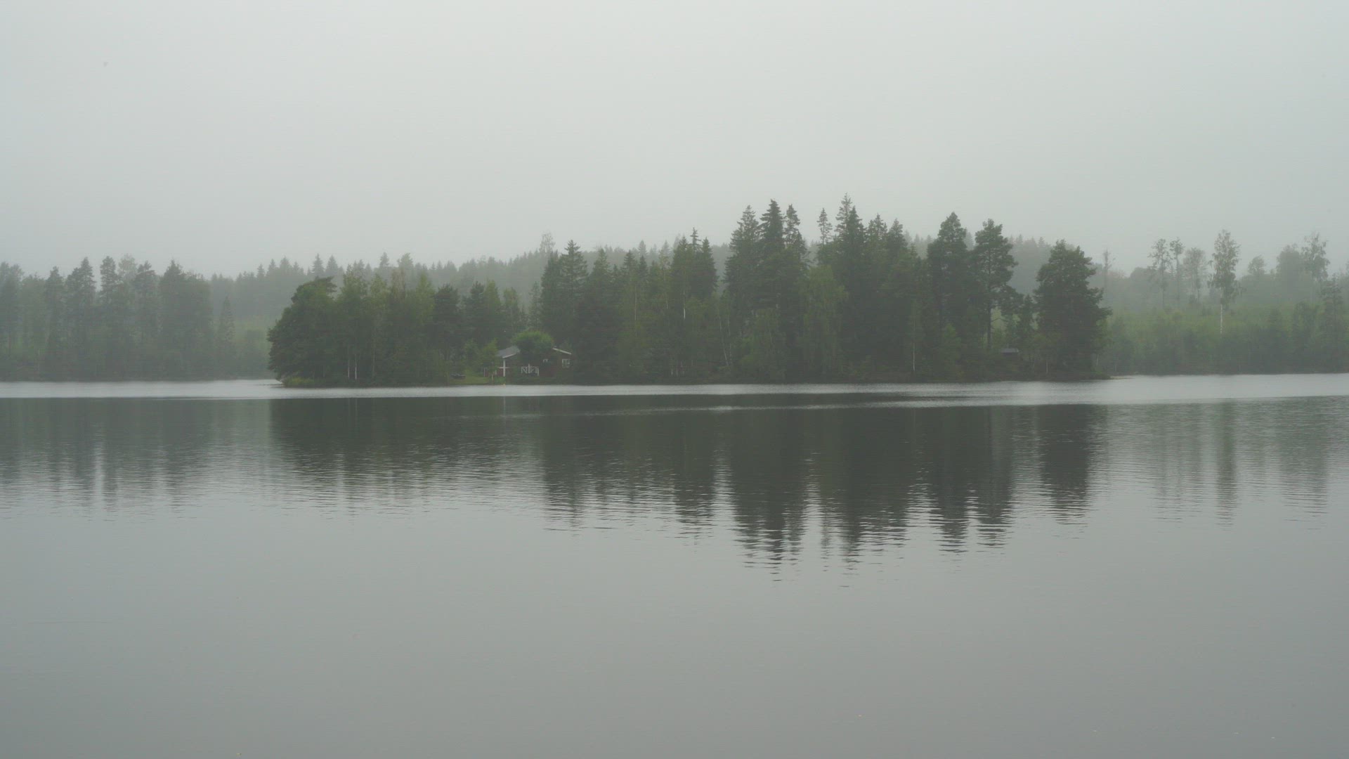 view over lake in misty foggy weather - distand red cottage house among trees in forest