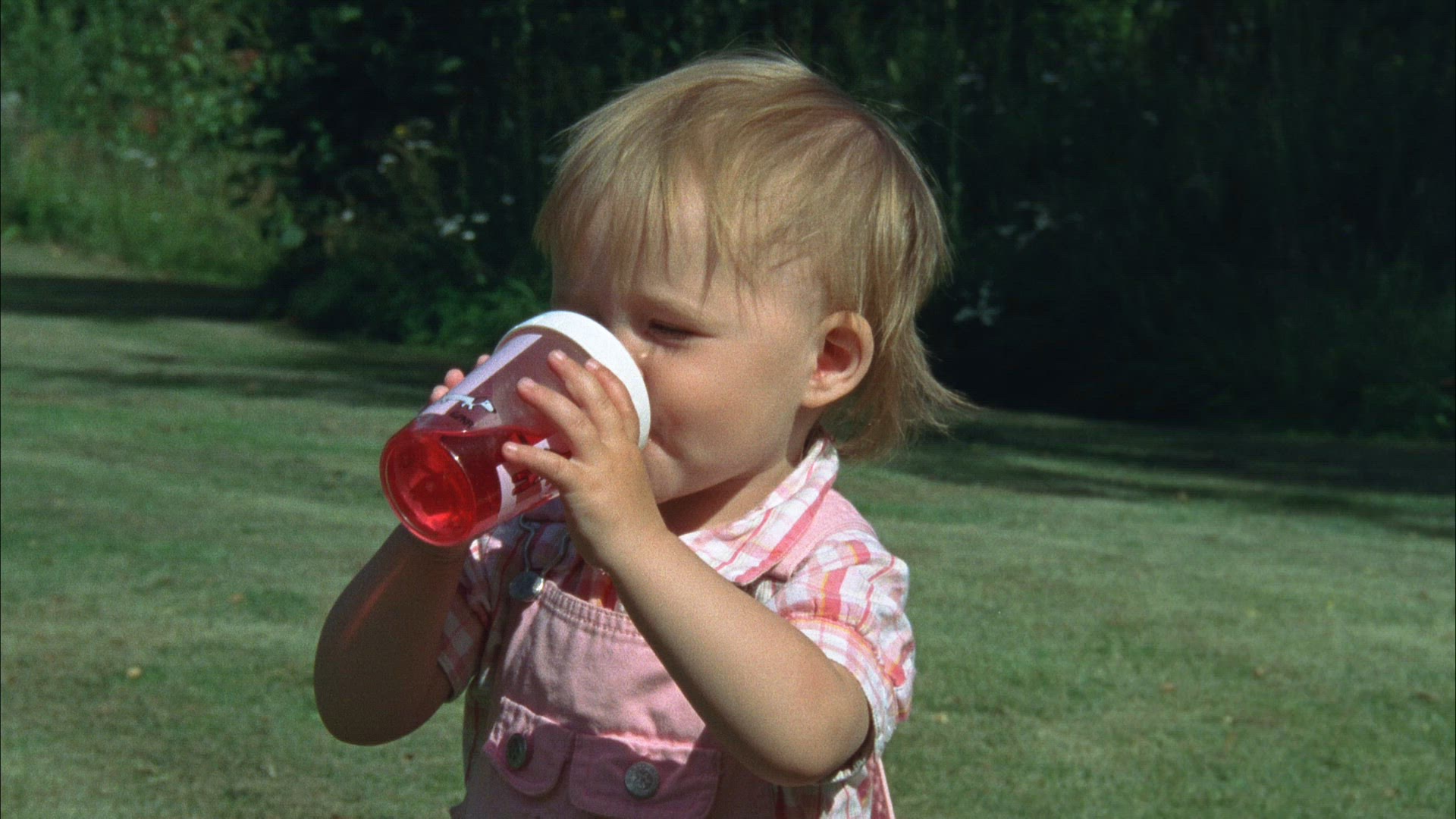 toddler drinking red lemonade from nursing bottle