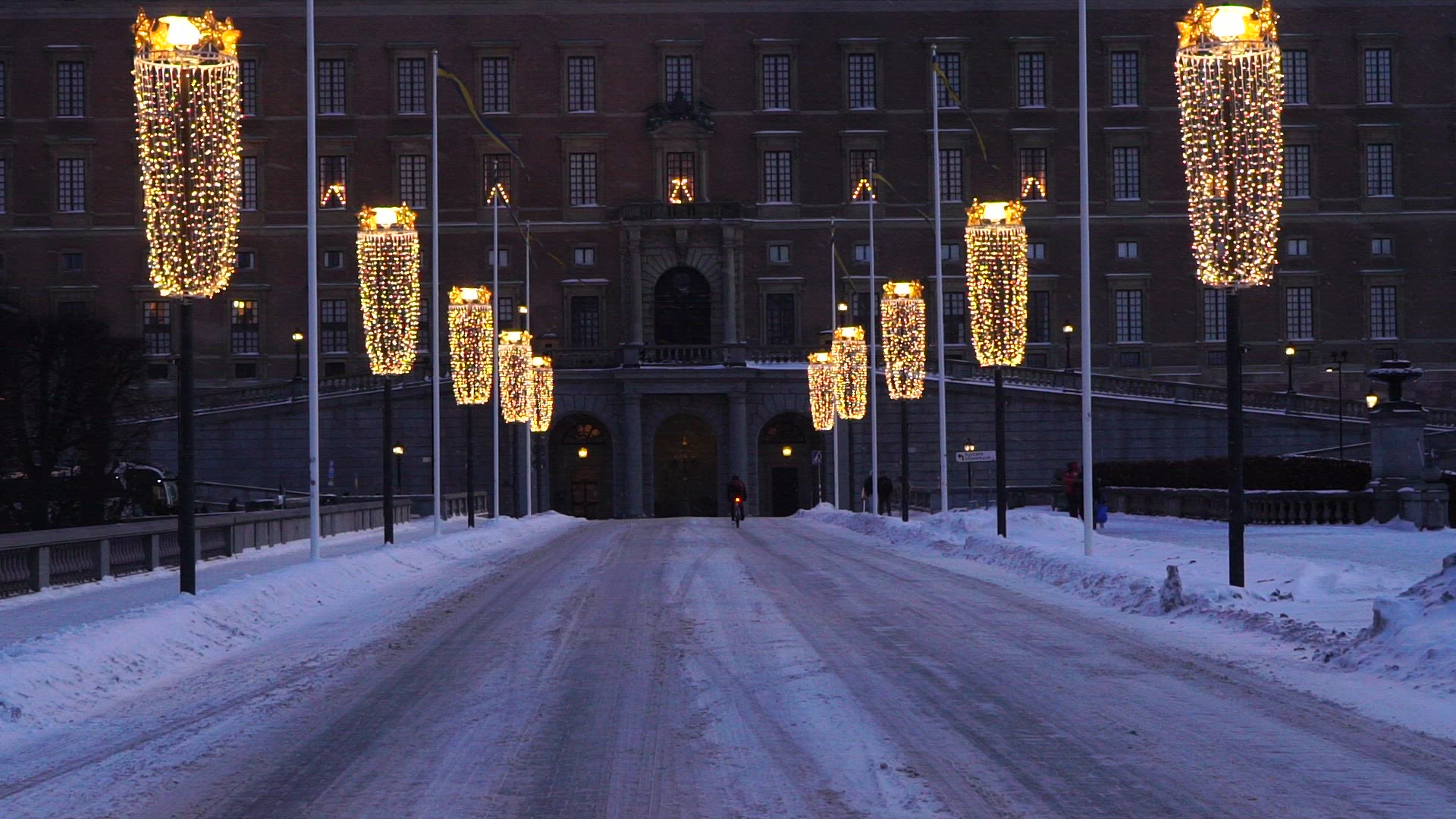 cyclist cycling on snowy illuminated street in stockholm - royal palace in background