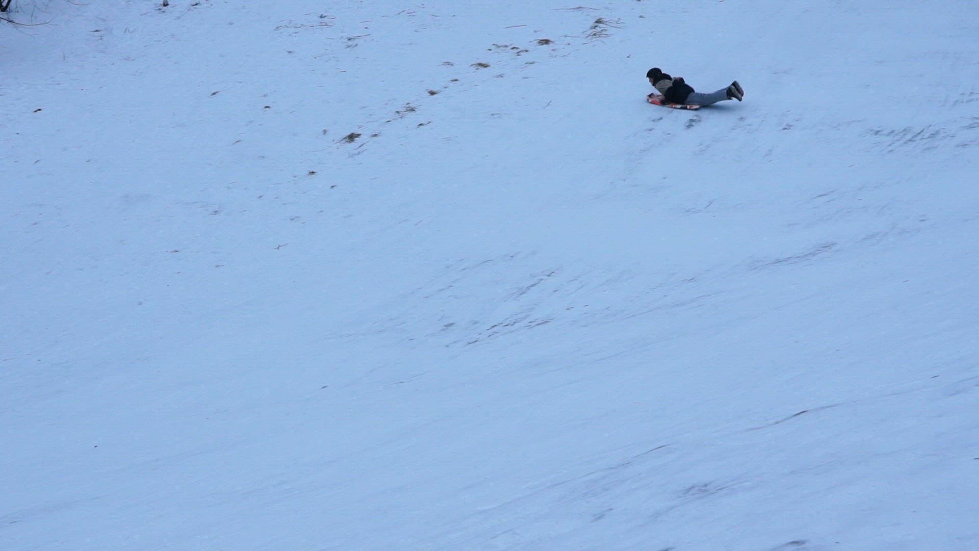 boy going down steep hill on plastic mattress - snow spraying - slowmotion shot