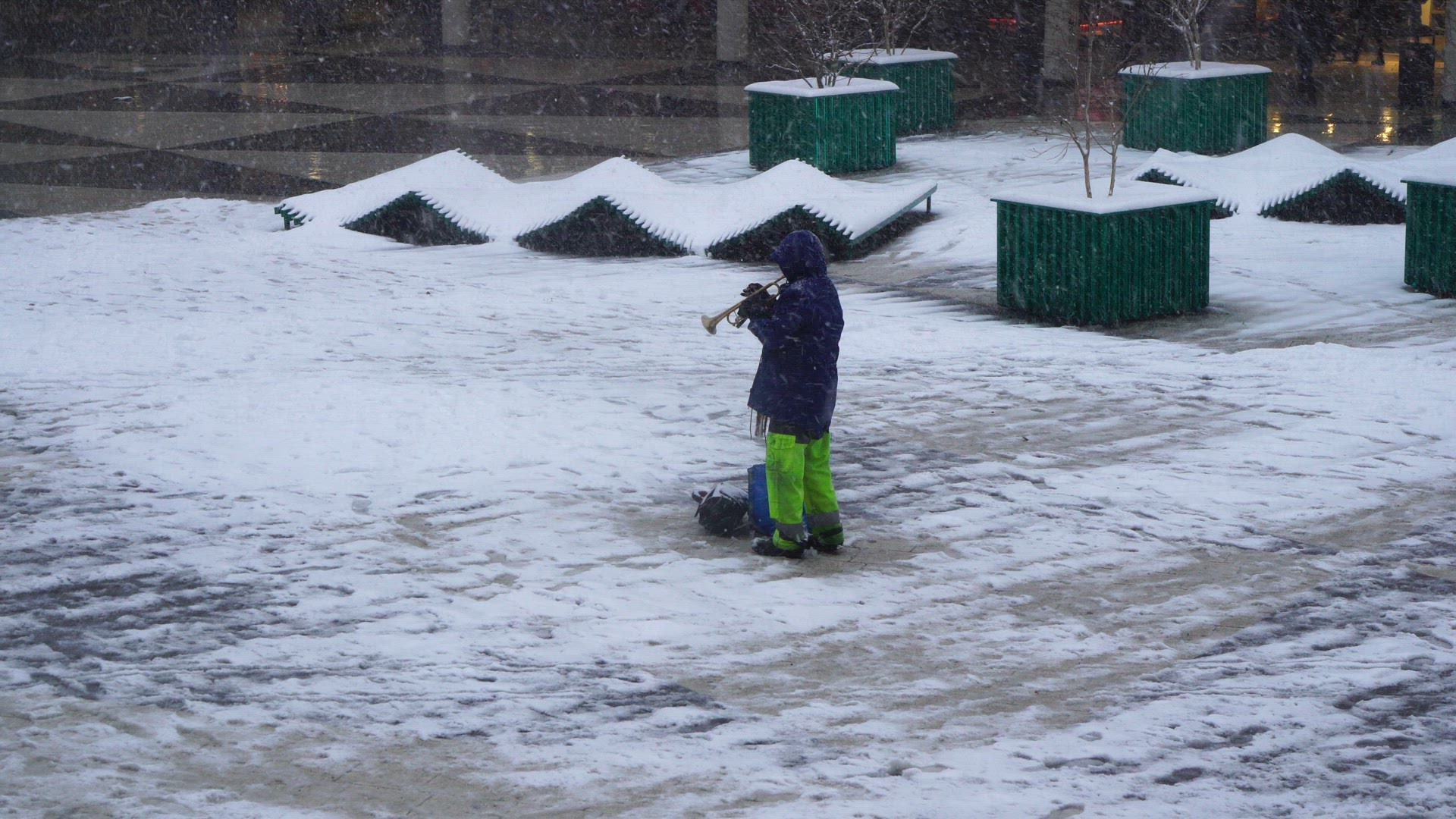 man standing in snowy weather on sergels torg in stockholm - playing trumpet in have snowfall