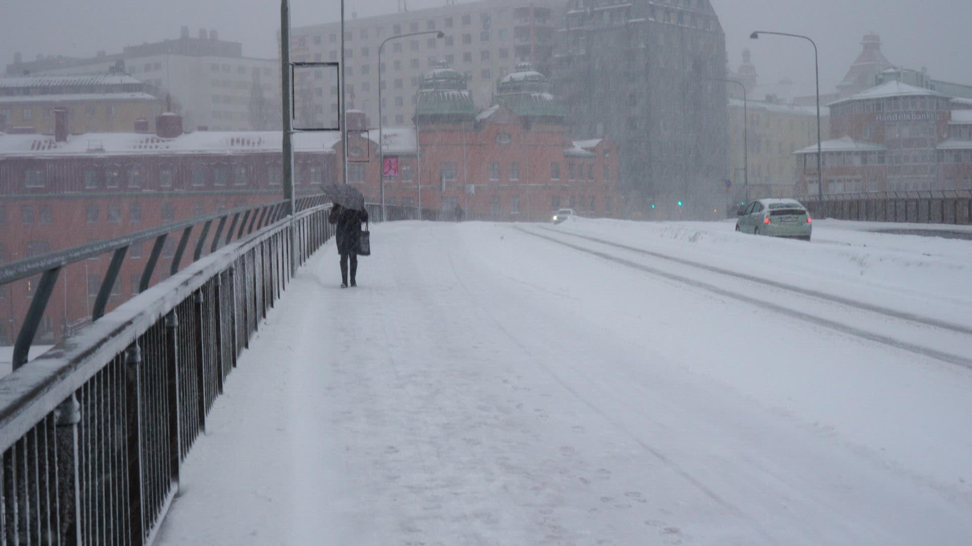 woman with umbrella walking on sidewalk in heavy snowfall and strong wind