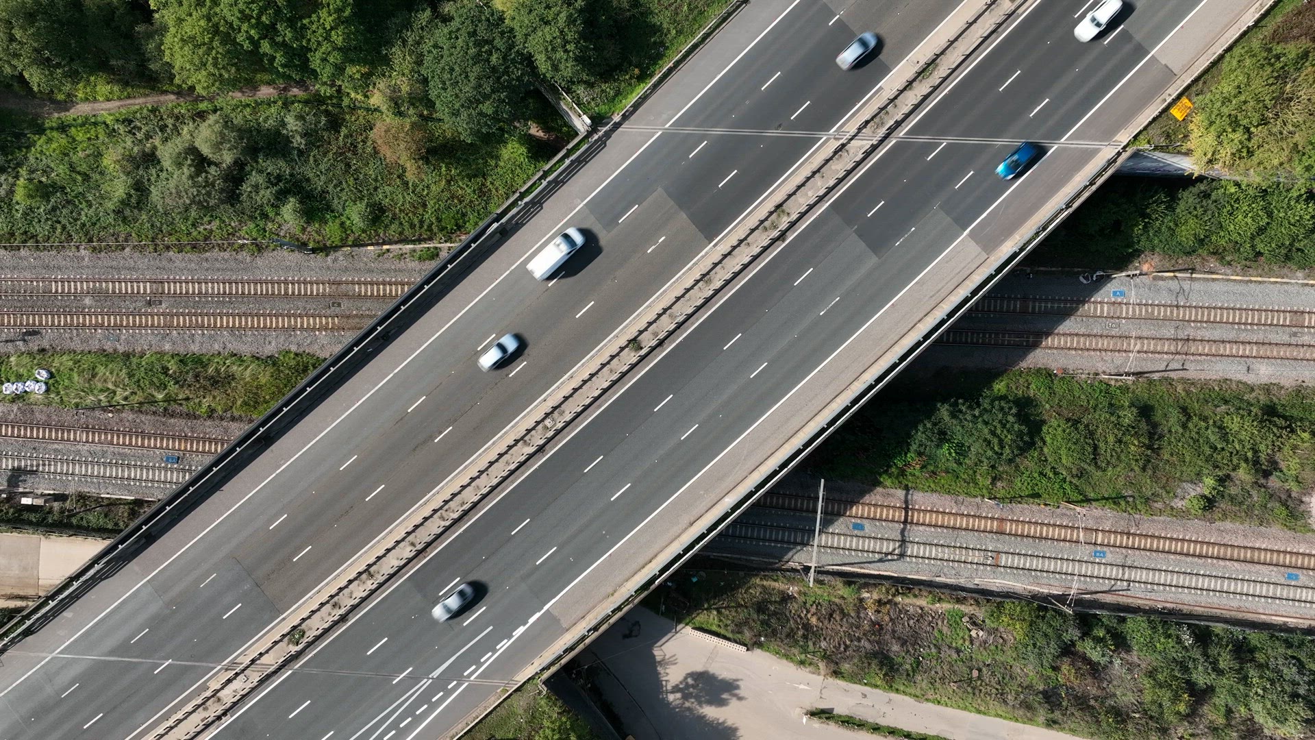 Commuter Train Speeding Under a Motorway in the UK Aerial View
