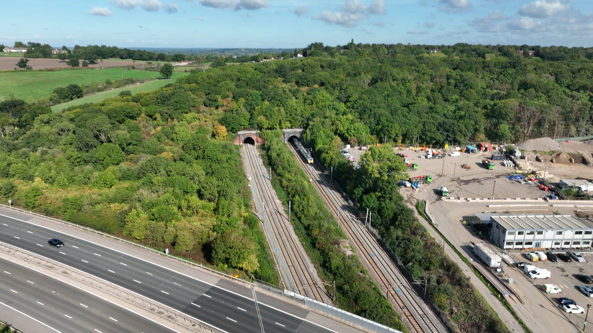Commuter Train Speeding Under a Motorway in the UK Aerial View