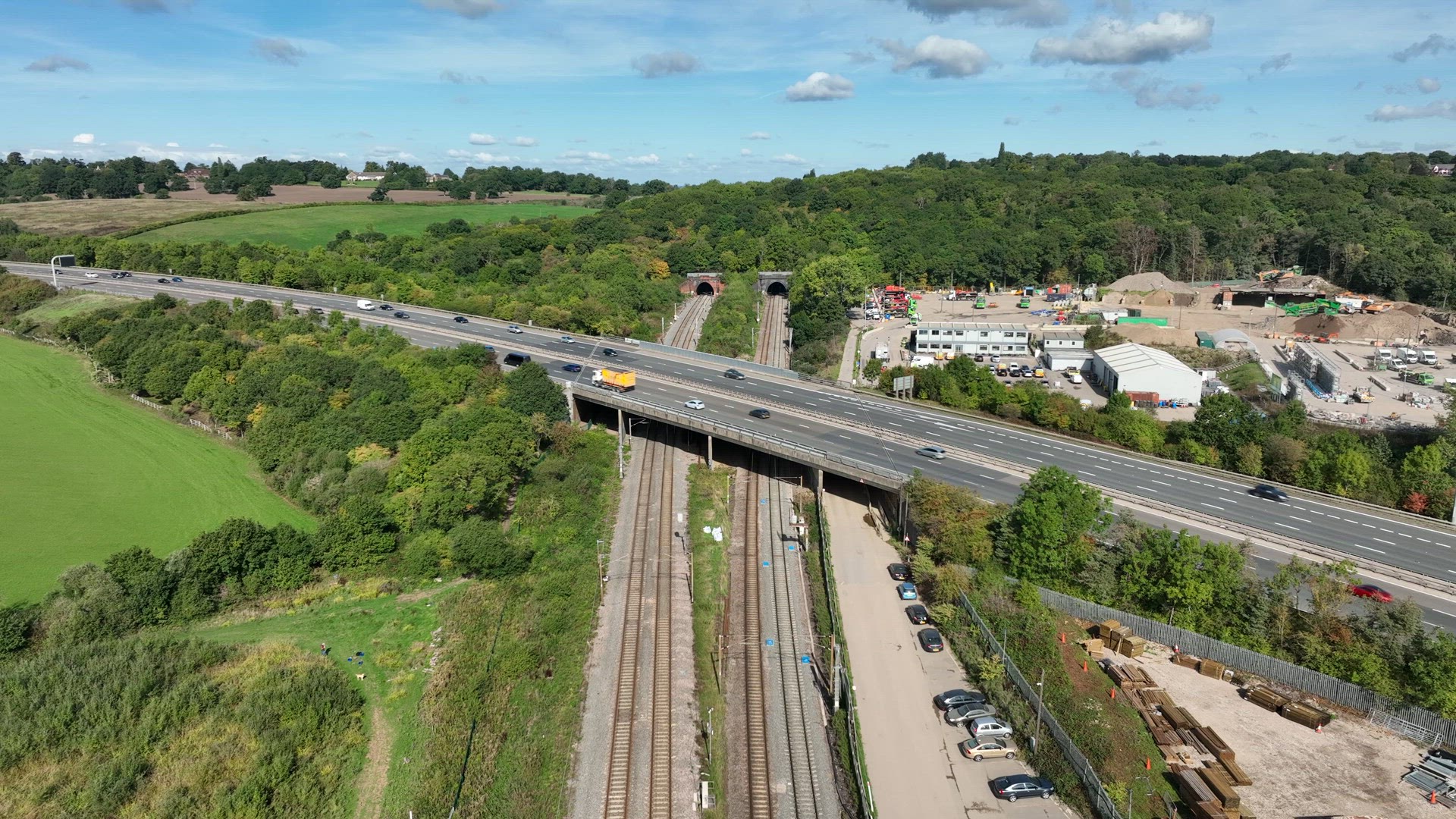 Commuter Train Speeding Under a Motorway in the UK Aerial View
