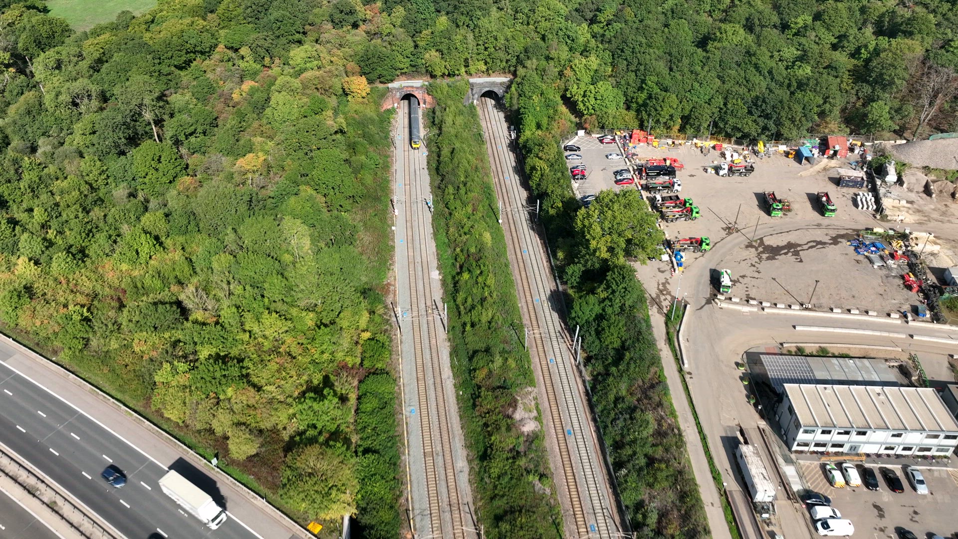 Commuter Train Speeding Under a Motorway in the UK Aerial View