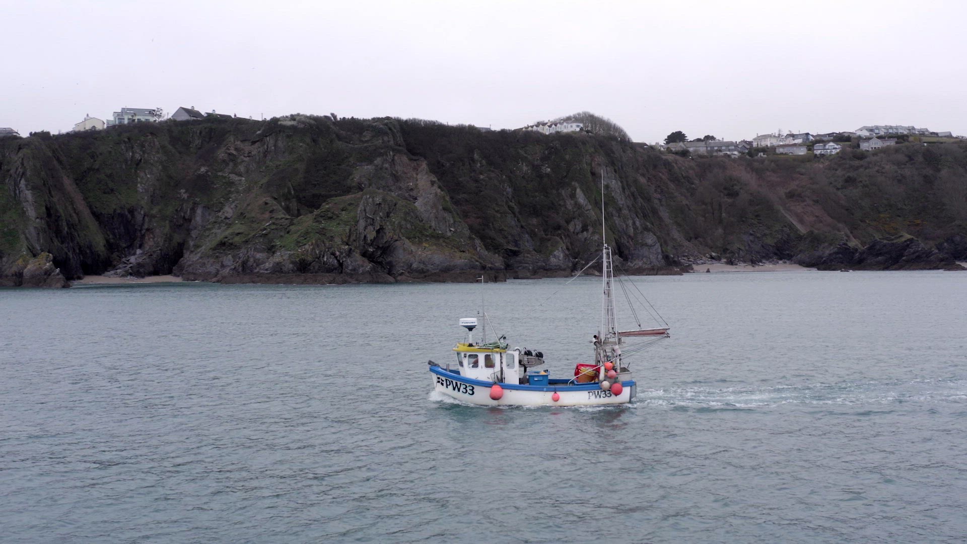 Fishing Boat Motoring at Sea With Tall Cliffs on a Grey Day