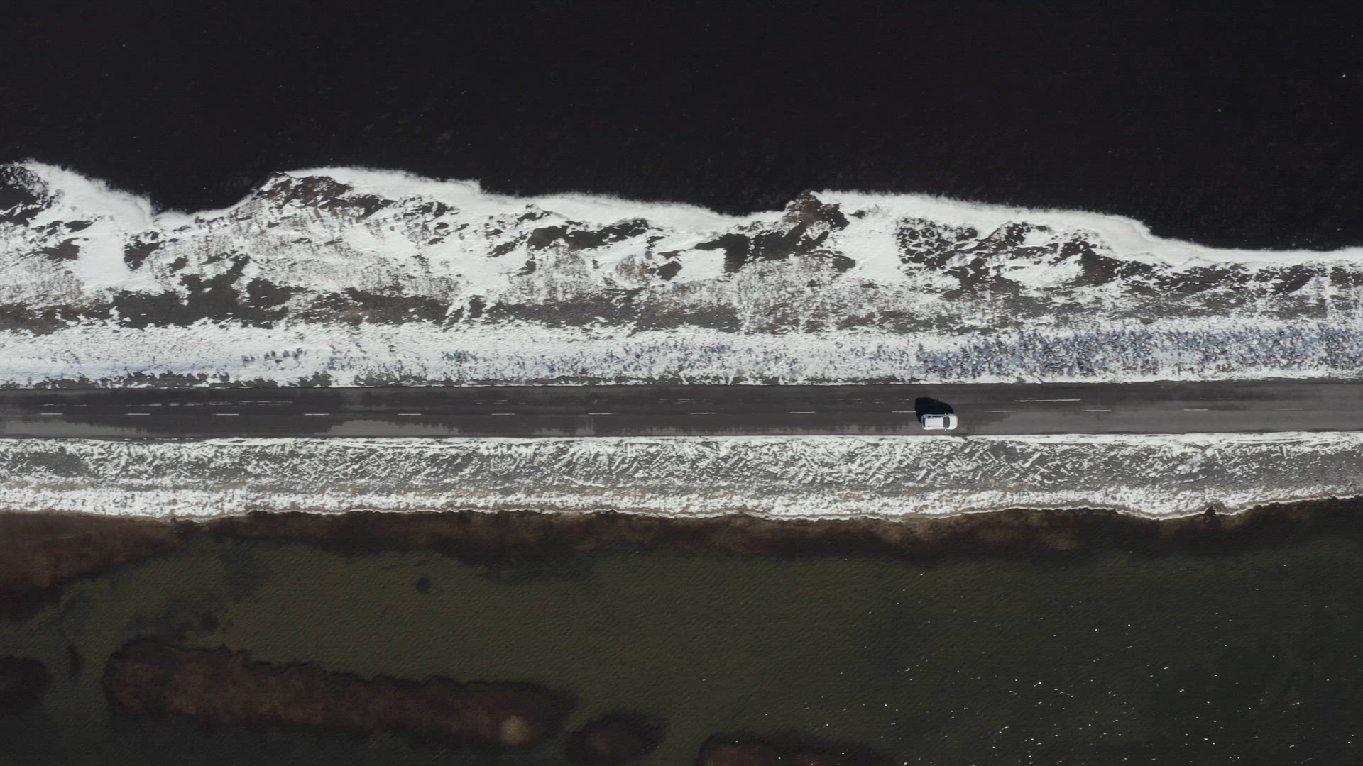 Bird's Eye View of a Car Driving Along a Narrow Road Crossing a Lake