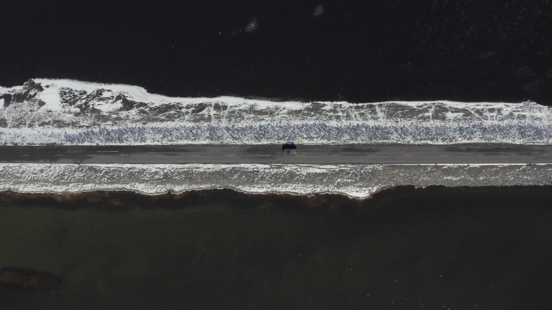 Bird's Eye View of a Car Driving Along a Narrow Road Crossing a Lake