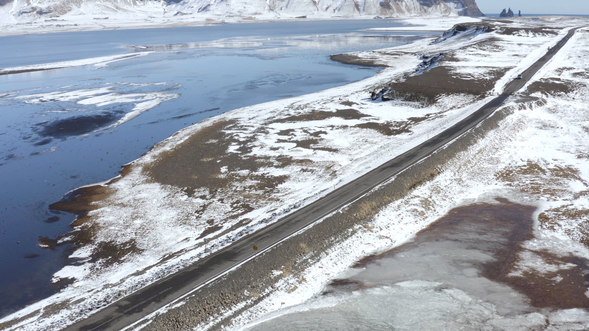 Cars Driving Along a Snowy Road With a Lake Surrounding