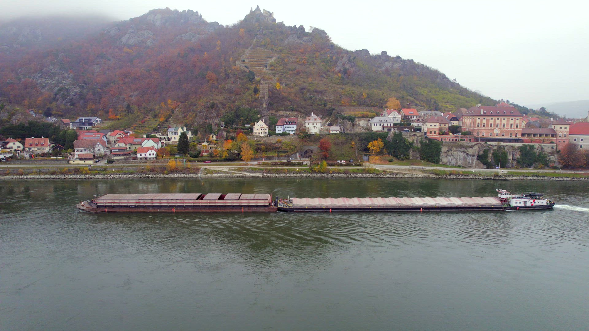 Cargo Pusher Boat on a River Transporting Cargo and Goods Past a Town