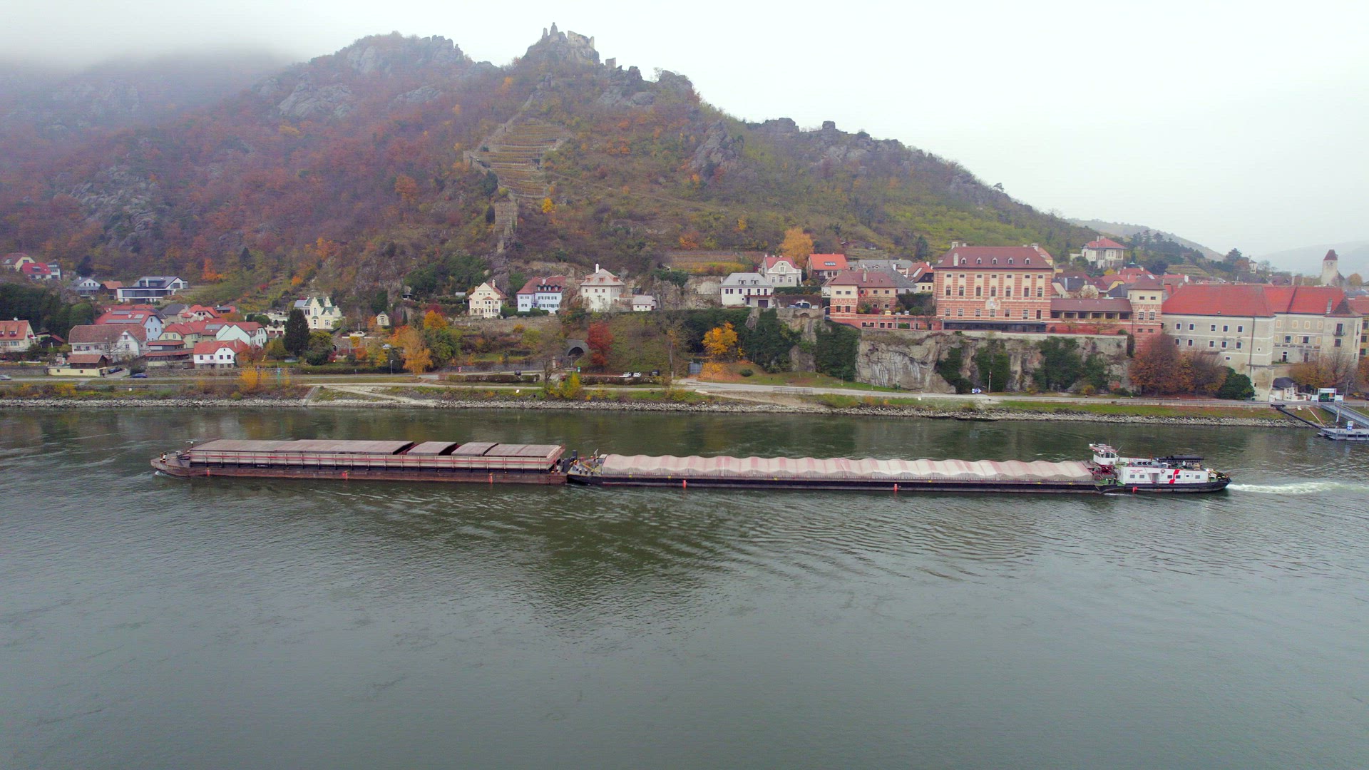 Cargo Pusher Boat on a River Transporting Cargo and Goods Past a Town