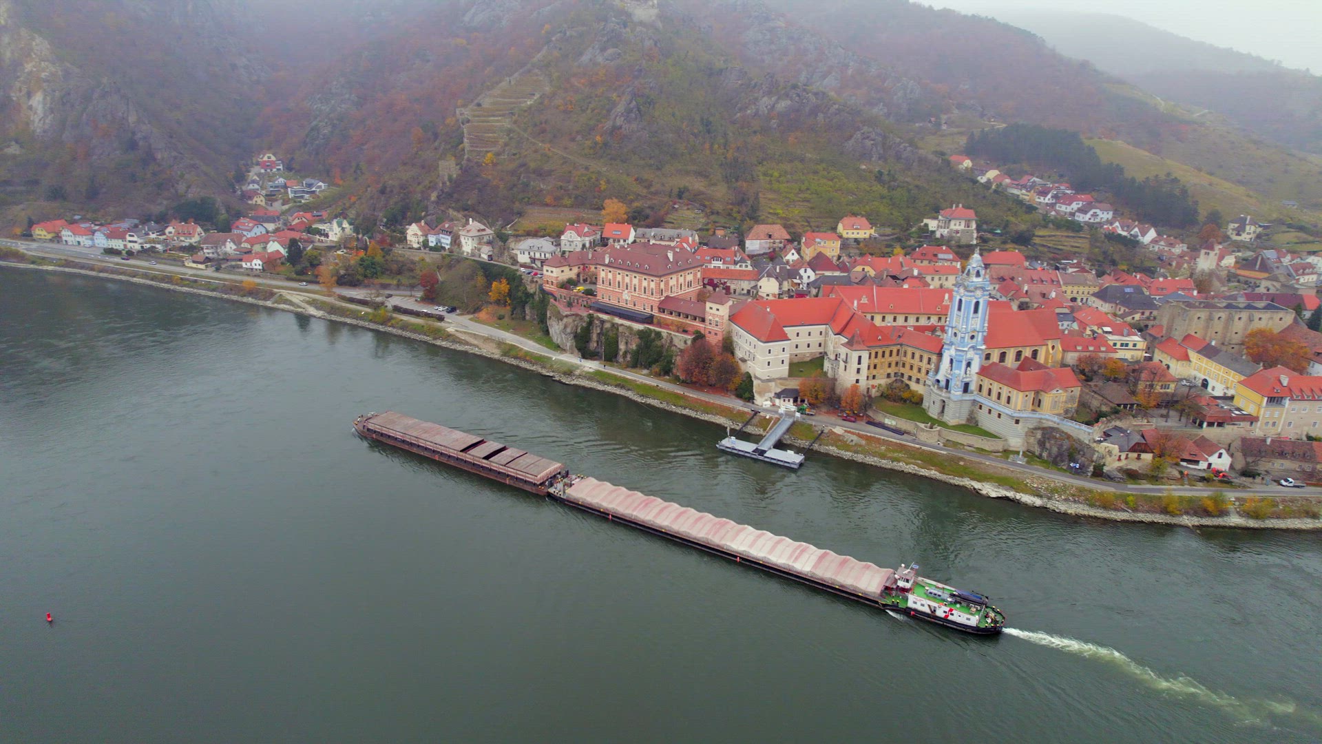 Cargo Pusher Boat on a River Transporting Cargo and Goods Past a Town