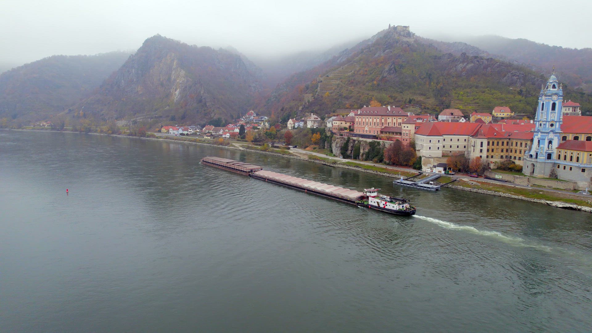 Cargo Pusher Boat on a River Transporting Cargo and Goods Past a Town