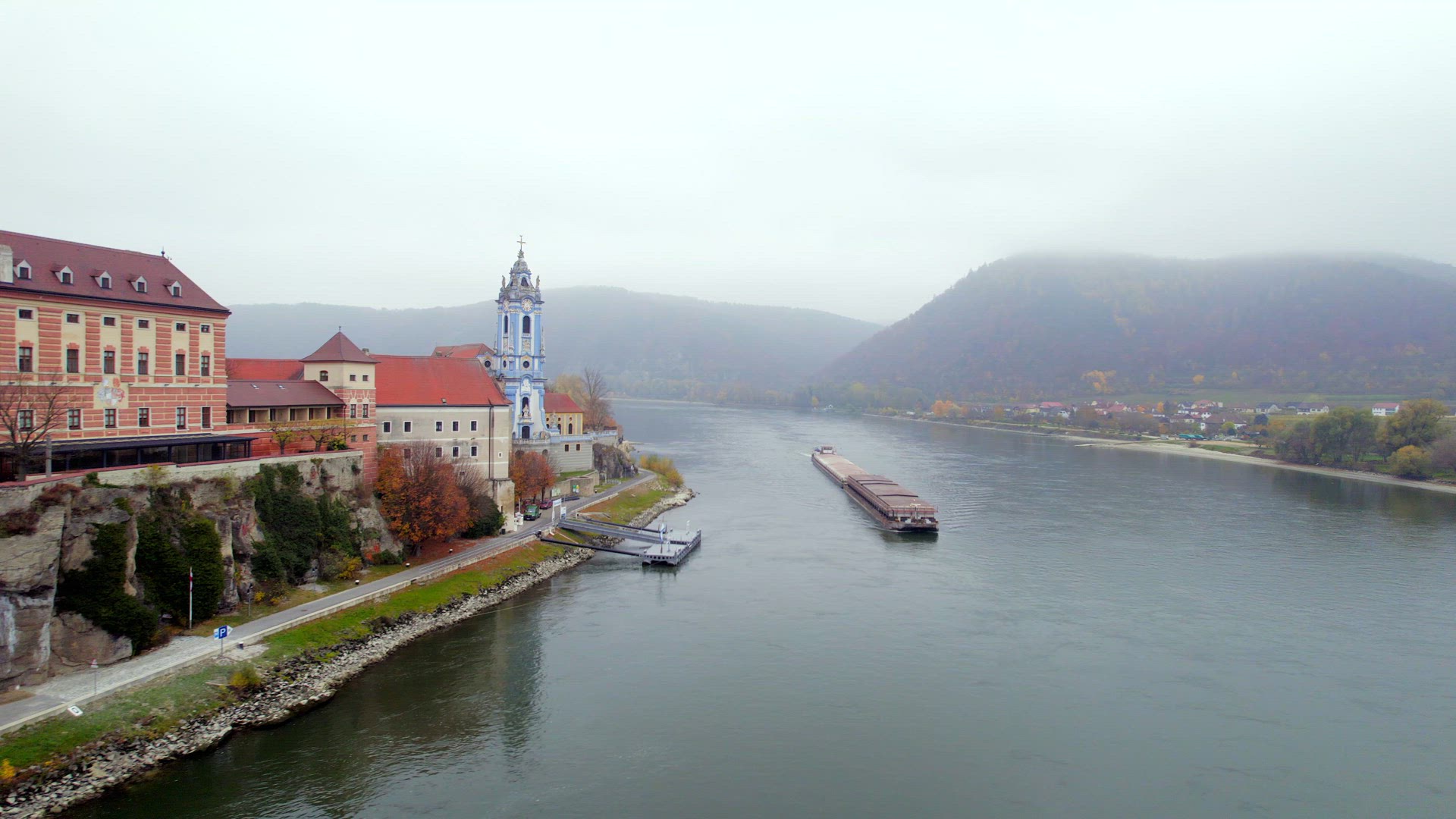 Cargo Pusher Boat on a River Transporting Cargo and Goods Past a Town