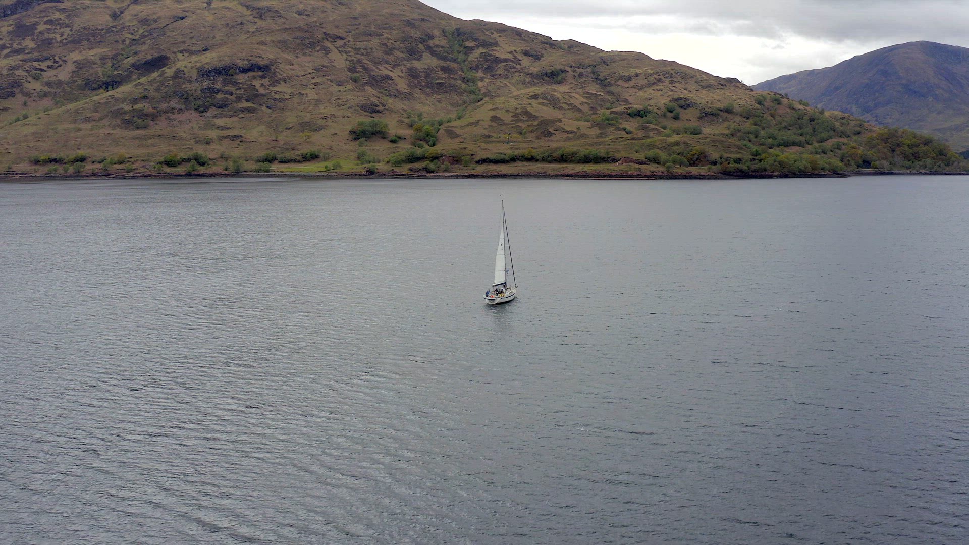 A Yacht Raising Sail Surrounded By Mountains and Forests in a Lake