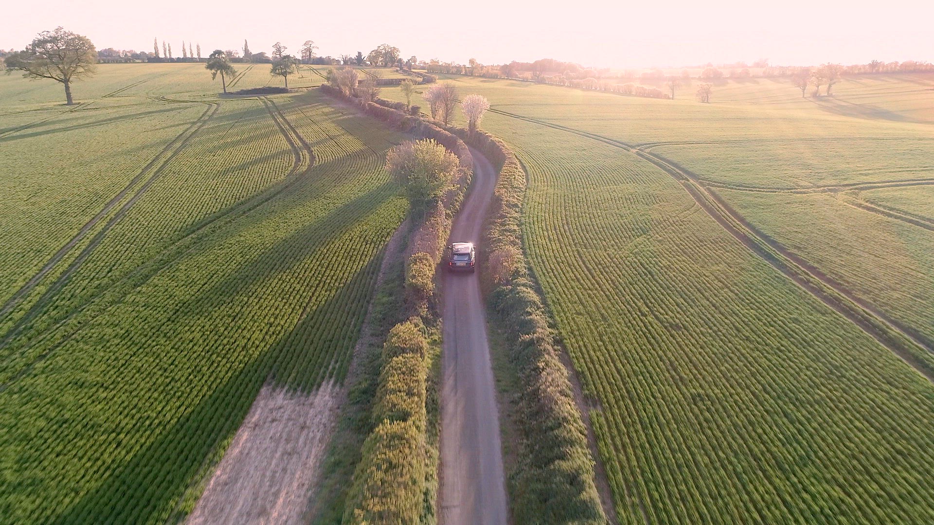 Aerial View of a Luxury SUV Driving Through a Country Lane in the Evening