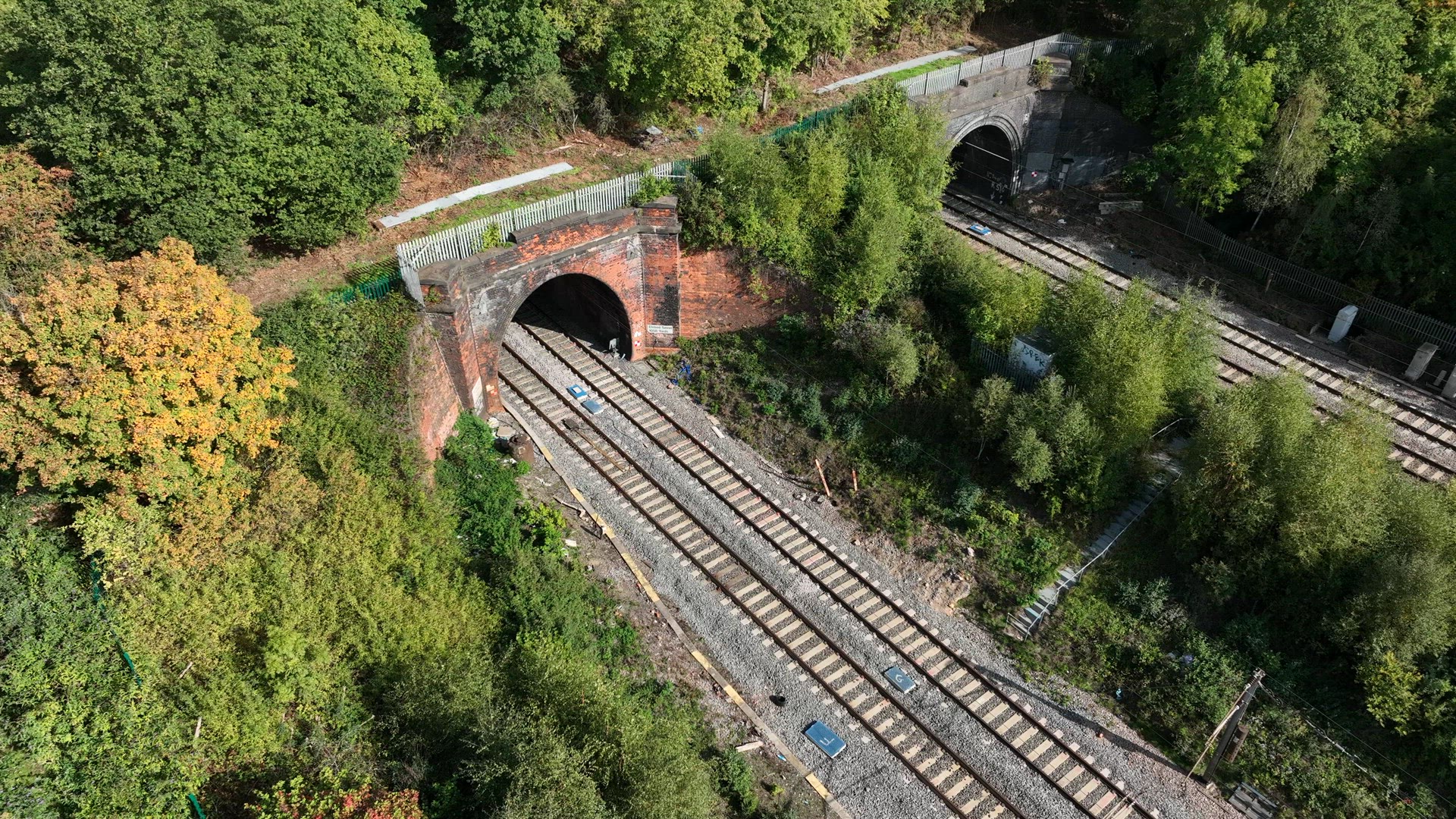 Commuter Train Speeding Under a Motorway in the UK Aerial View