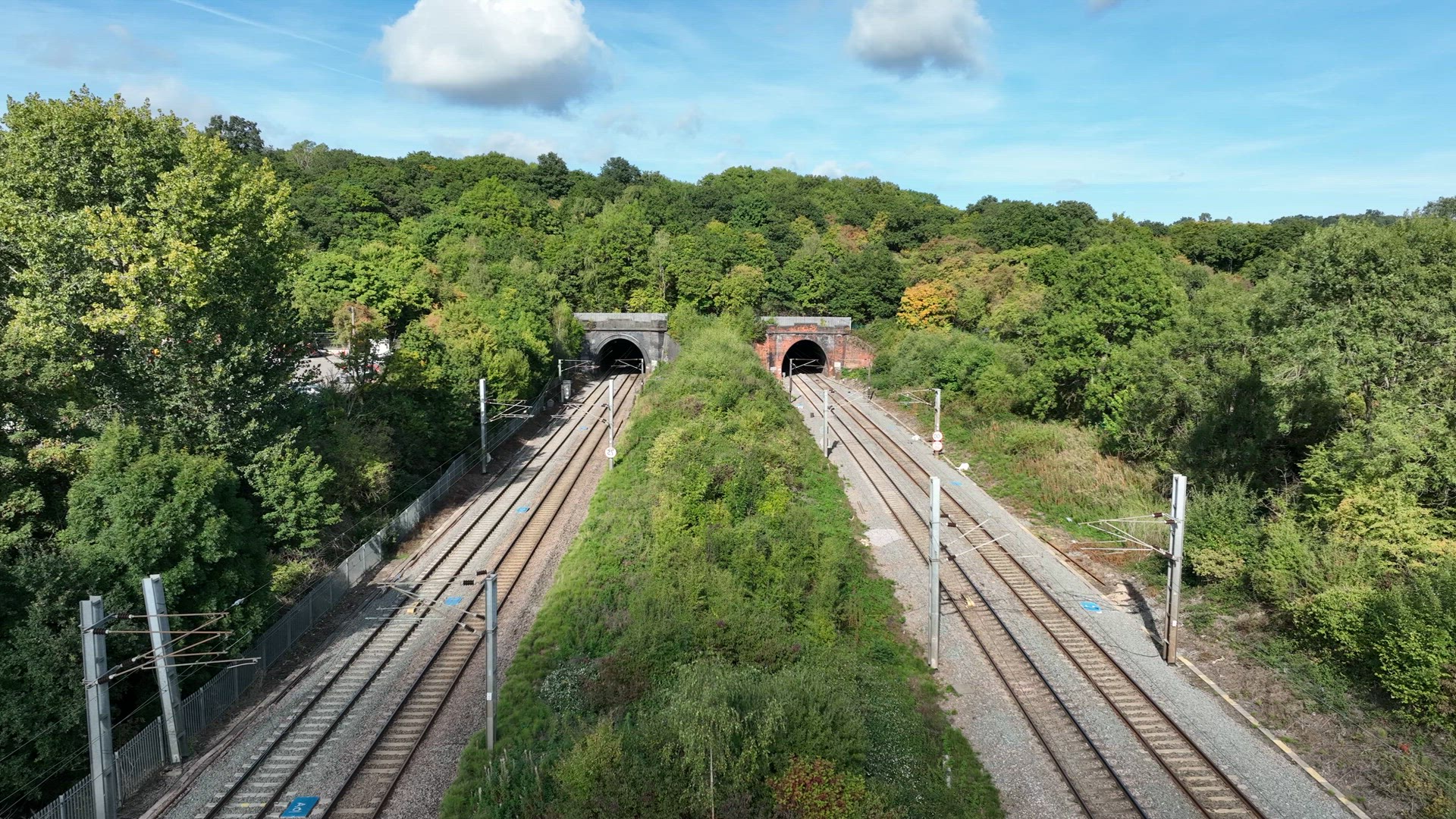 Commuter Train Speeding Under a Motorway in the UK Aerial View