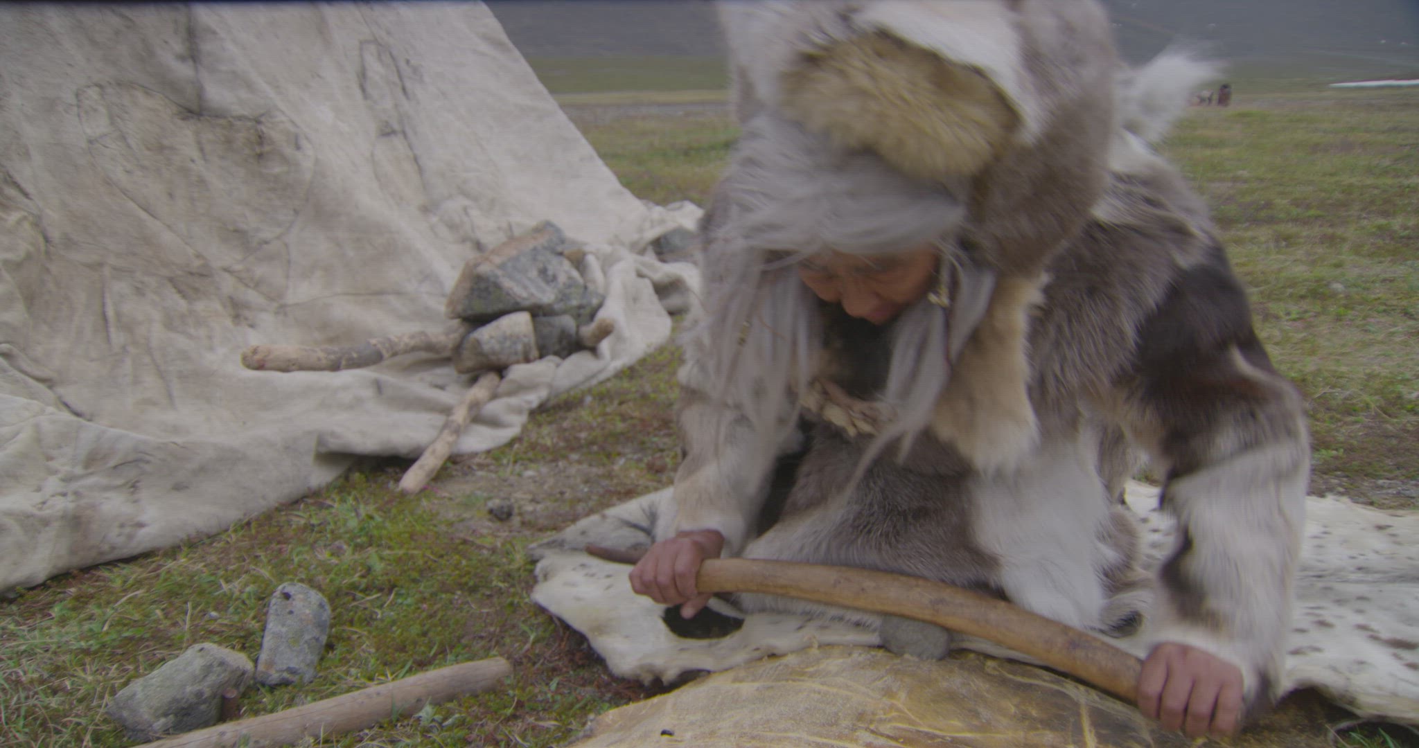 nomadic hunter outside hut preparing animal fur
