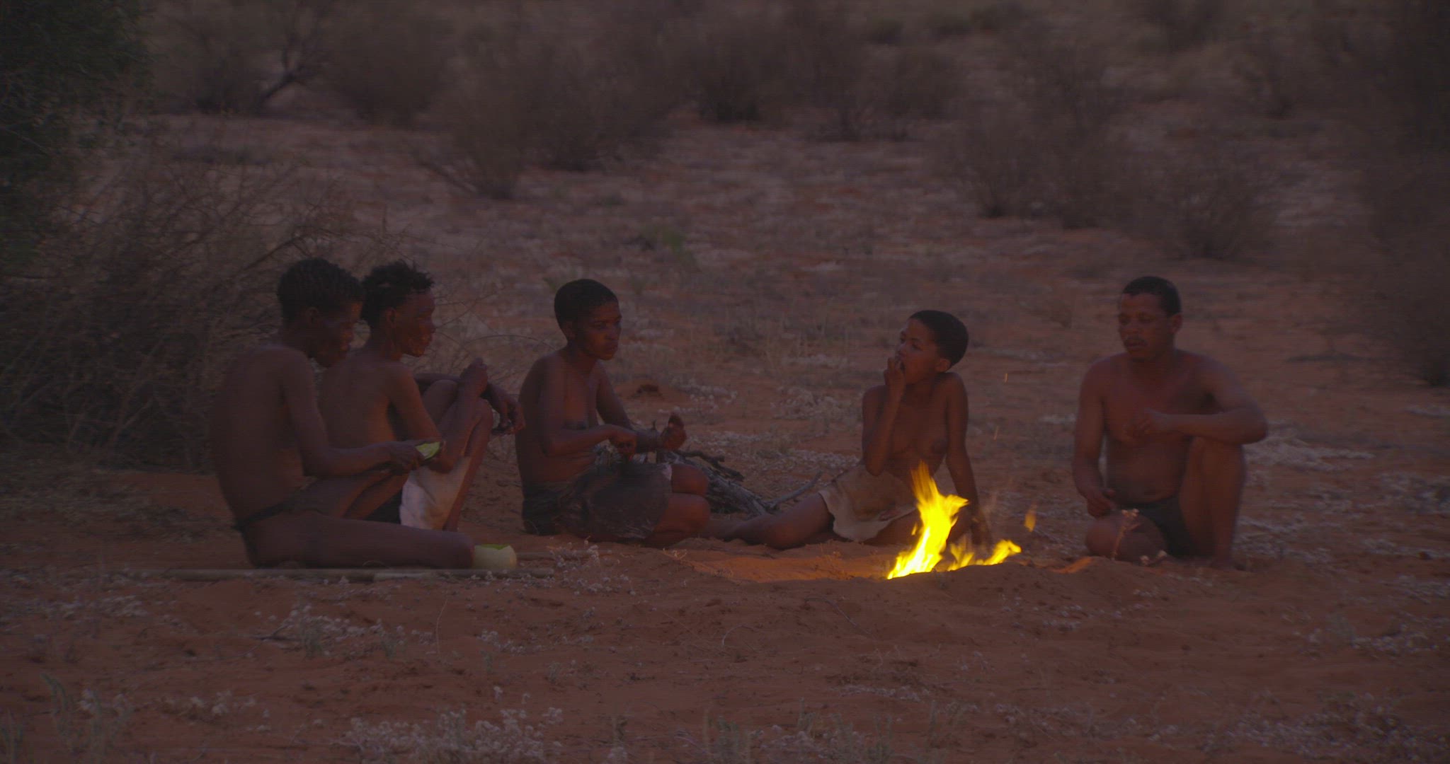 early humans seated around a fire eating