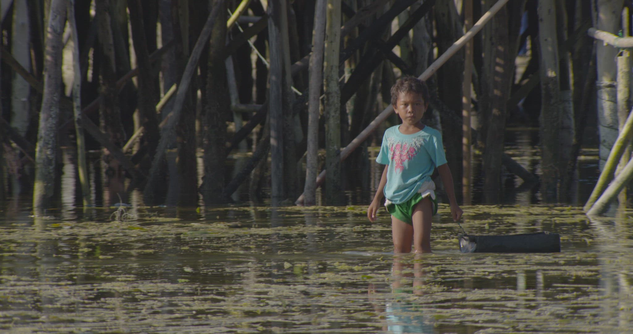 young boy walking in water with toy boat