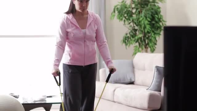 Asian woman exercising with resistance bands while watching television