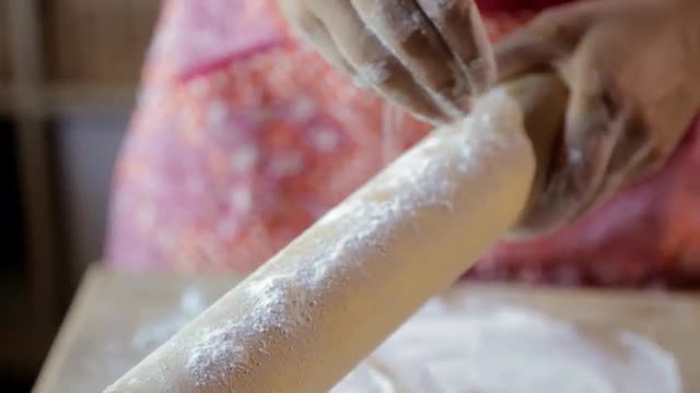 Hispanic woman sprinkling flour on rolling pin