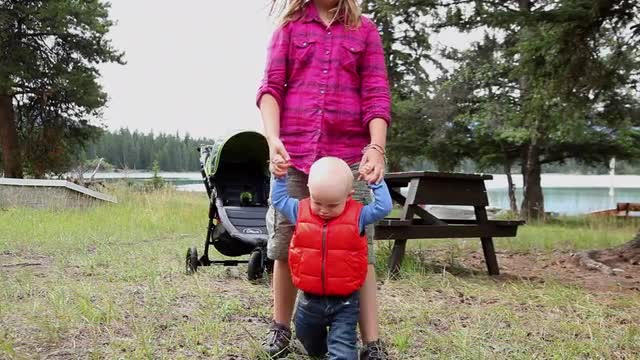 Caucasian girl helps baby boy walk in park