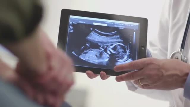 Caucasian obstetrician showing couple ultrasound on digital tablet