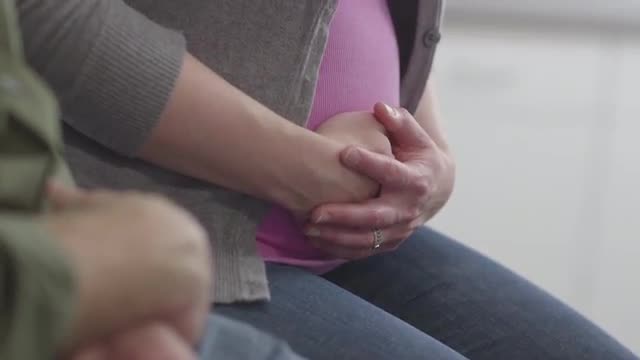 Pregnant Caucasian couple holding hands and stomach