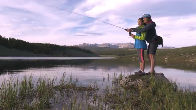 Mother teaching daughter fly fishing in river