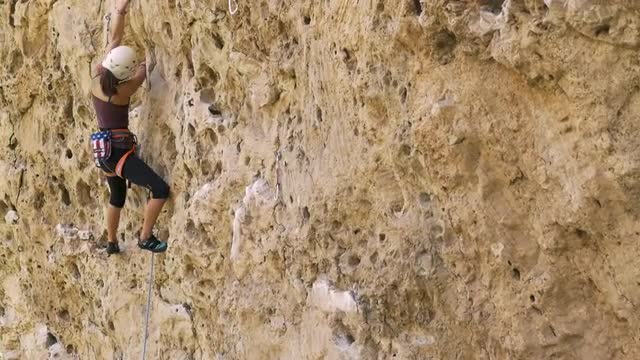 Mixed race girl rock climbing and fastening belay rope to boulder